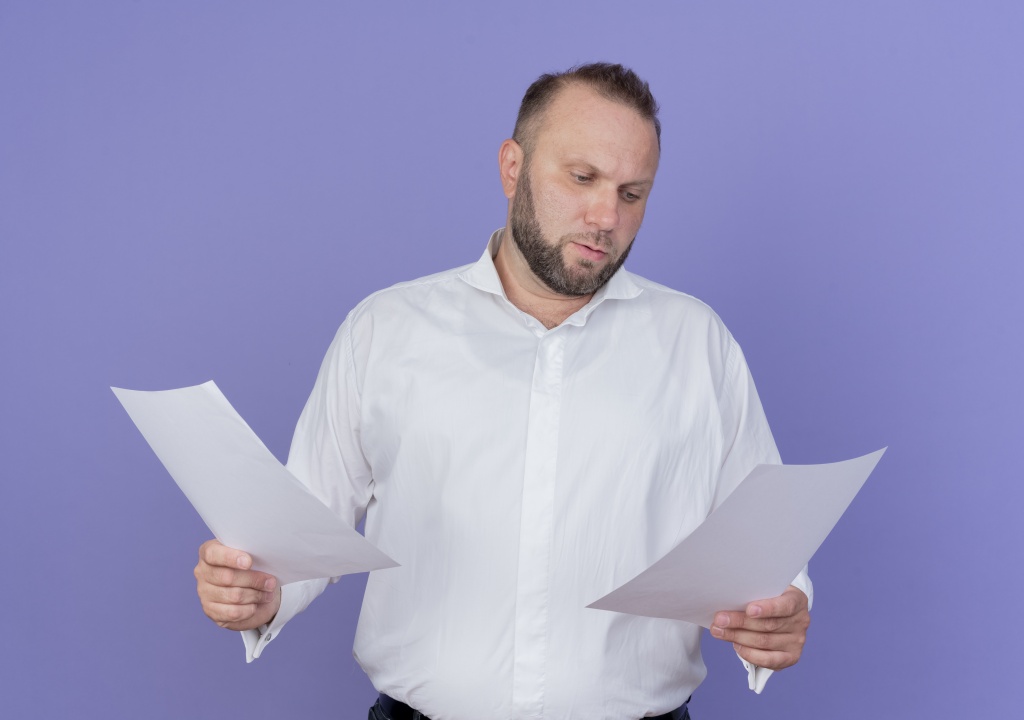bearded-man-wearing-white-shirt-holding-blank-sheets-paper-looking-them-with-serious-face-standing-blue-wall.jpg мужчина